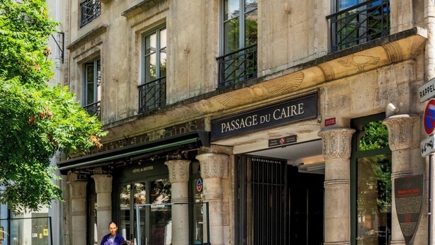 Ein Gebäude im klassischen Stil, ein Café namens 'Passage du Caire' mit Außenbestuhlung und ein Schild mit der Aufschrift 'RAPPEL' (kein Parken).