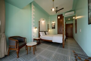 A bedroom with a bed, a wooden chair, a small table, and patterned floor tiles.
