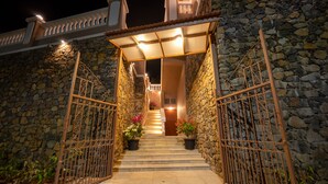 A stone-walled entrance with a metal gate, a staircase leading to a door, and potted plants.