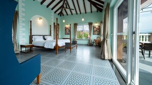 A spacious bedroom with a large bed, a sitting area with a chair and table, and a view through a large window.