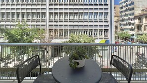 A balcony with a table and chairs, a potted plant, and a view of a building with multiple windows. - Éclair: Lovely 2BD apt perfect for families (Thessaloniki)