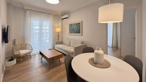 A modern living room with a sofa, coffee table, and dining table. There is a chair, a lamp, and a painting on the wall. - Éclair: Lovely 2BD apt perfect for families (Thessaloniki)