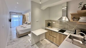 Una habitación de hotel moderna con una cama, una pequeña kitchenette y un baño visible a través de una puerta de vidrio.