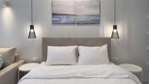 Un dormitorio moderno con una cama, dos mesitas de noche, un buró, un cuadro colgado en la pared y lámparas colgantes.