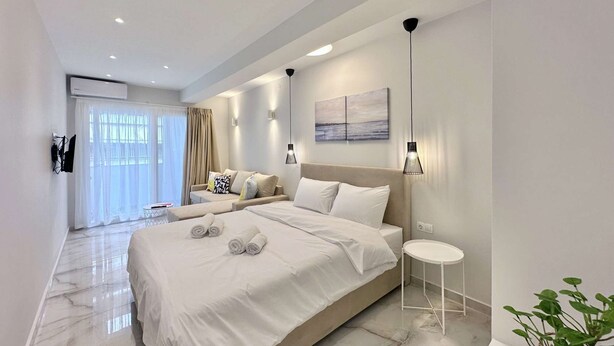 Un dormitorio moderno con una cama grande, un sofá, una mesita y una planta en maceta.