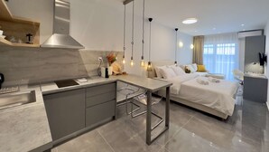 Ein modernes Hotelzimmer mit Kochnische, einem Bett mit weißer Bettwäsche und einem Badezimmer mit Spiegel und Waschbecken.