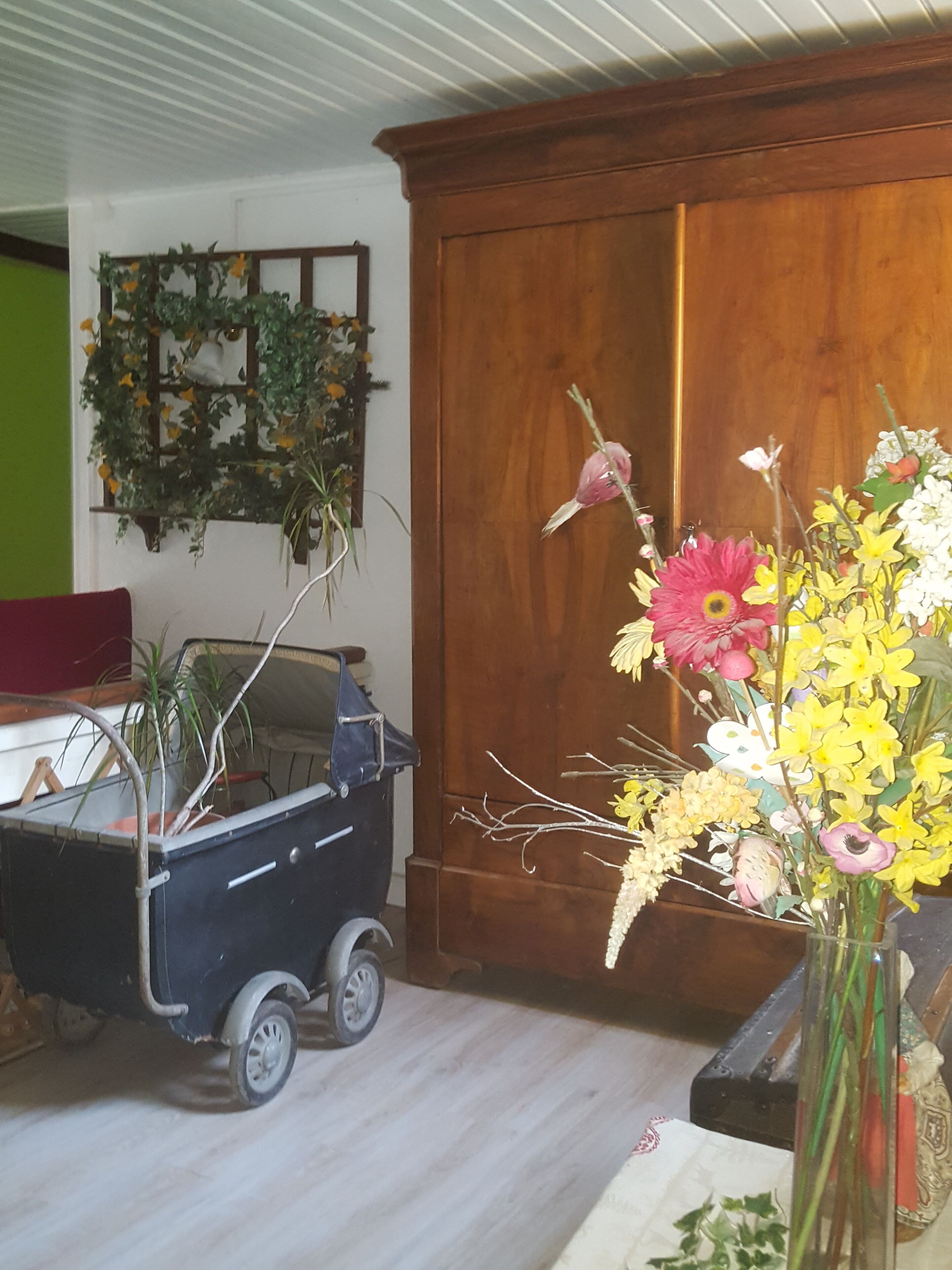 Una habitación con un armario de madera, un carrito pequeño con plantas y un adorno floral en la pared.