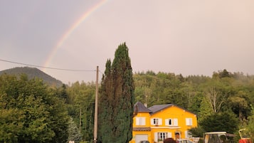 Una casa amarilla con un camino de entrada, coches aparcados y un tractor.