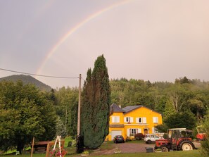 A yellow house with a driveway, parked cars, and a tractor. - Gîte Forestier du Moulin (Raon-sur-Plaine)