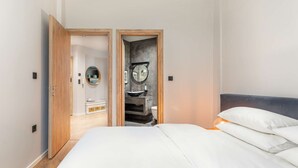 A bedroom with a bed, a wooden door, a bathroom with a sink and toilet, and a mirror. - Estelle: Grand 2-BD + 2 bath center apt (Thessaloniki)
