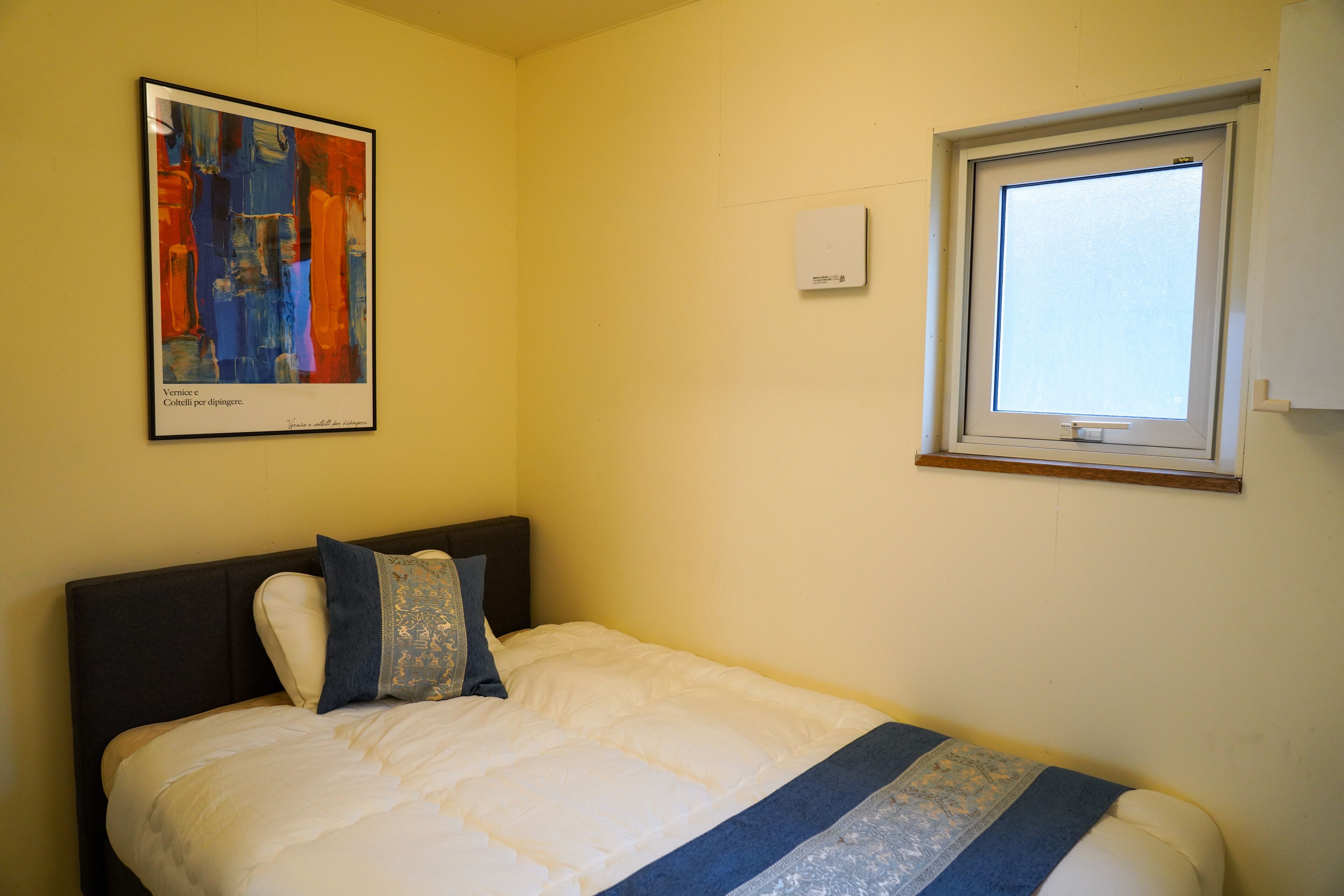 Quarto com cama, janela e uma obra de arte emoldurada na parede.