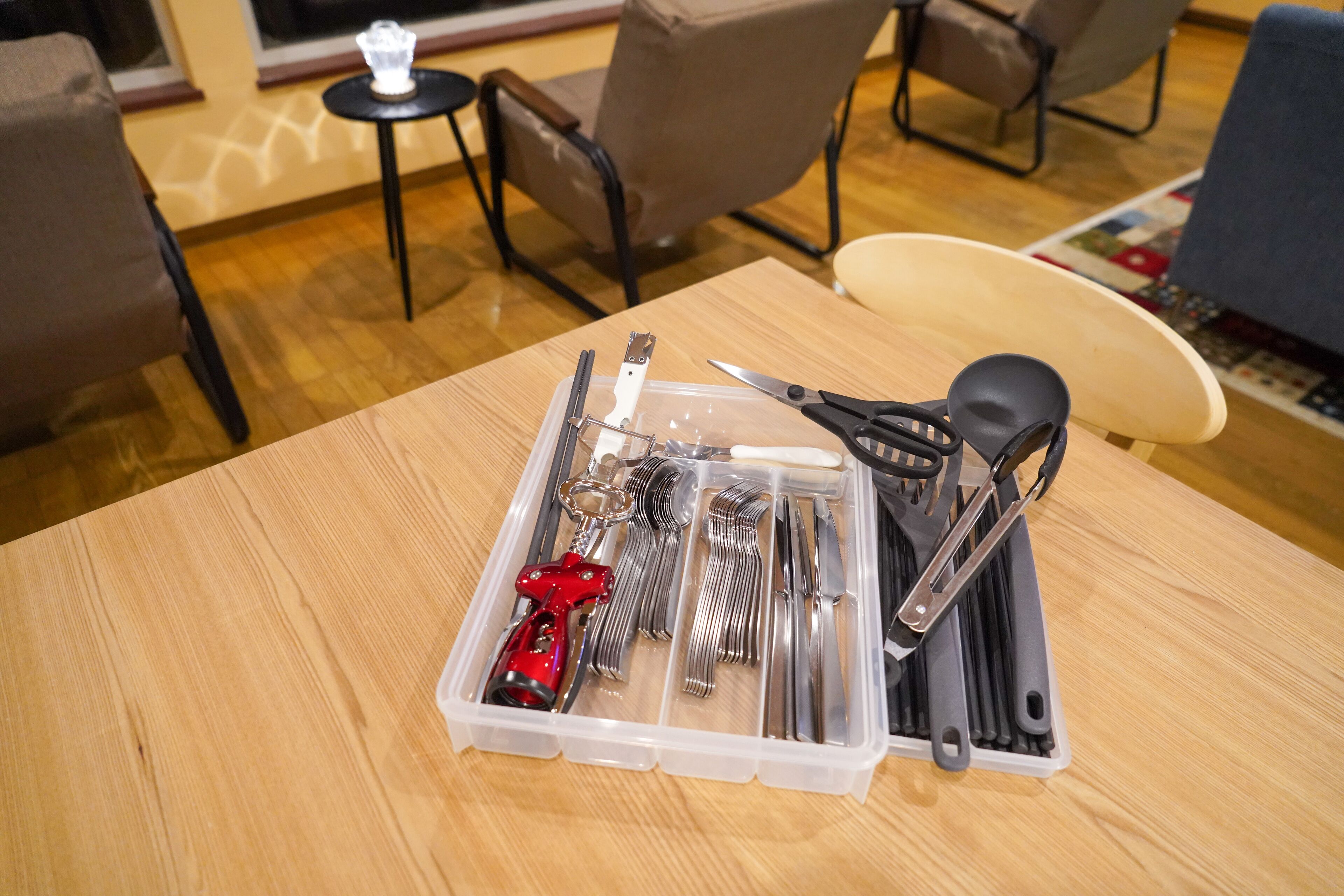 A wooden table with a plastic container holding various utensils.