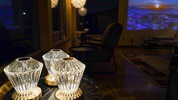 A room with a large window, a projection screen displaying a sunset, and three illuminated glass lamps on a table.