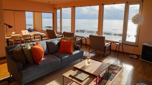 A modern living room with a large gray sofa, a wooden coffee table, and a view of the water through large windows. - Nesaki Native (Hakodate)