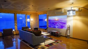 A modern living room with a sofa, a small table, and a projector screen displaying a scenic view. - Nesaki Native (Hakodate)