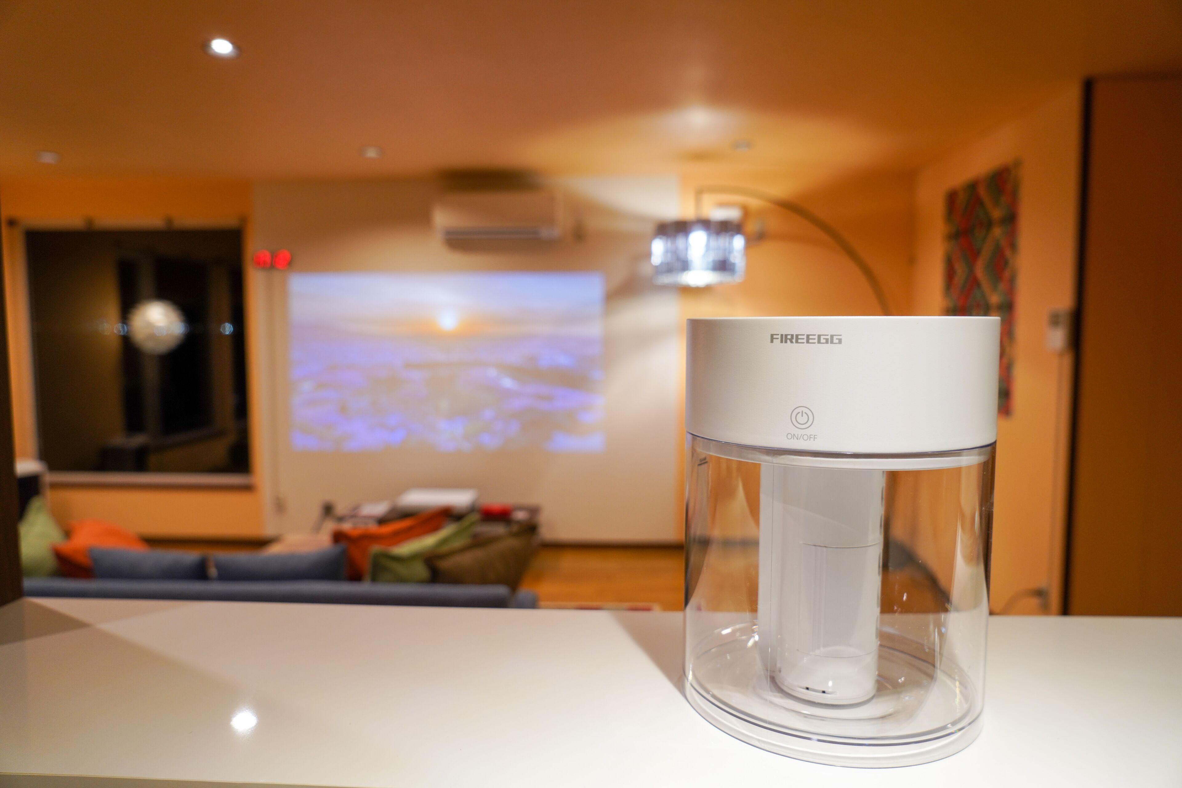 A FIEEGG water dispenser on a table in a room with a projection screen displaying a cityscape.