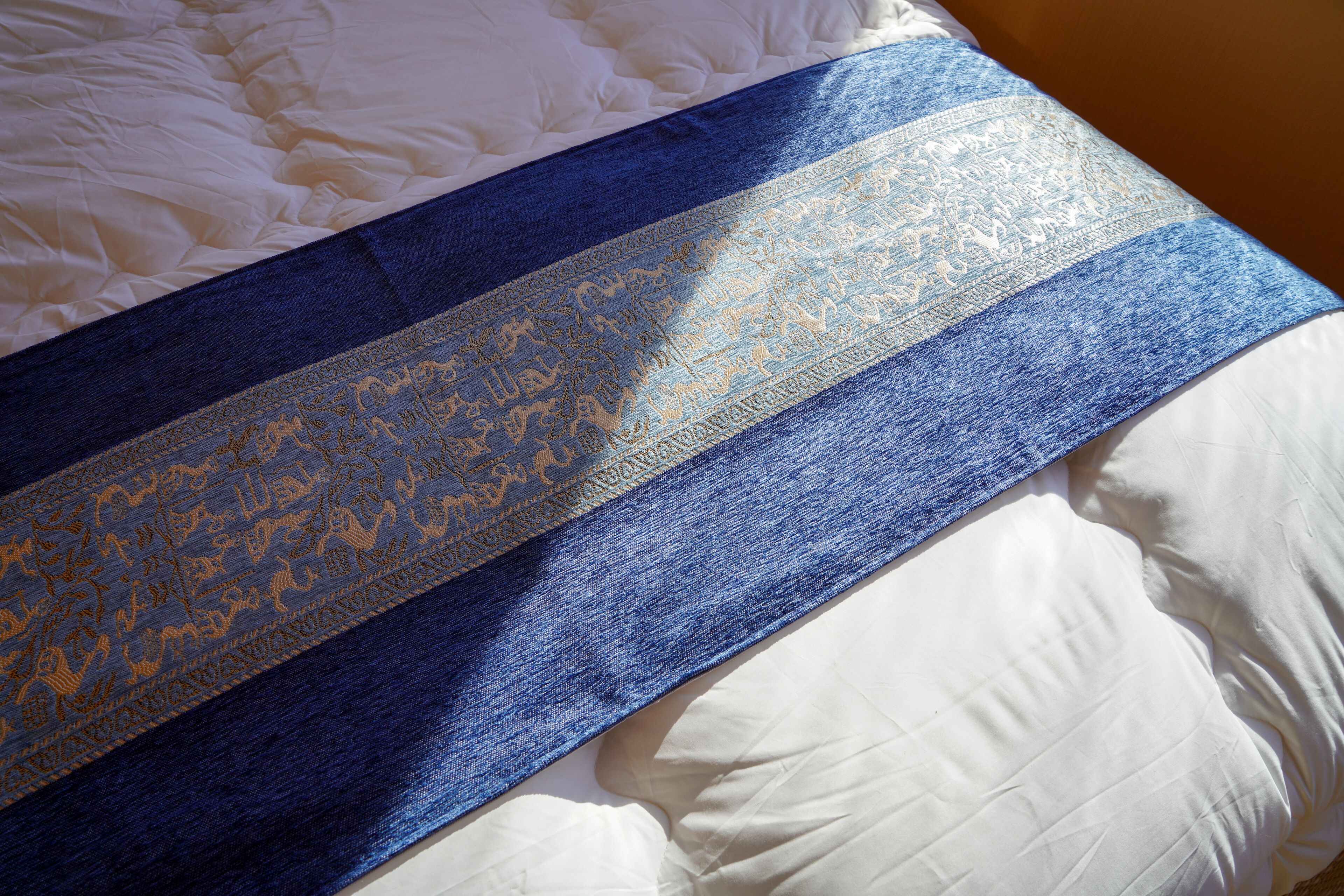 A bed with a white duvet and a blue and gold patterned blanket.
