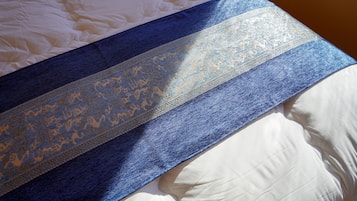 A bed with a white duvet and a blue and gold patterned blanket.