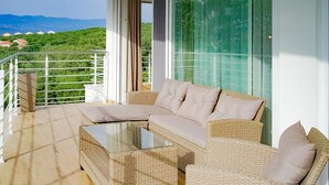 Un balcón con mobiliario de mimbre, una mesa de vidrio y vistas a colinas verdes.
