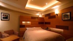 A hotel room with a bed, a sofa, a small table, and a wall-mounted light fixture. - HOTELm - Adults Only (Matsudo)