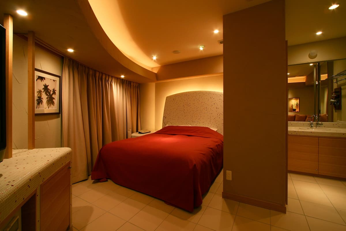 A bedroom with a large bed, a bedside table, a mirror, and a bathroom visible through an open door.