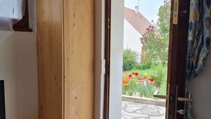 An open door leading to a garden with red flowers and a tiled patio. - Studio Indépendant Refait à Neuf (Villiers-Saint-Denis)