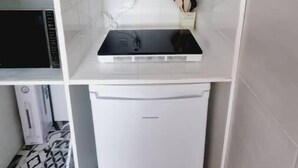 A compact kitchen with a built-in microwave, a small refrigerator, and a shelf with a plant. - Studio Indépendant Refait à Neuf (Villiers-Saint-Denis)