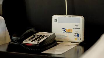 A hotel room with a desk featuring a landline phone, a 3BB broadband router, and a power outlet.