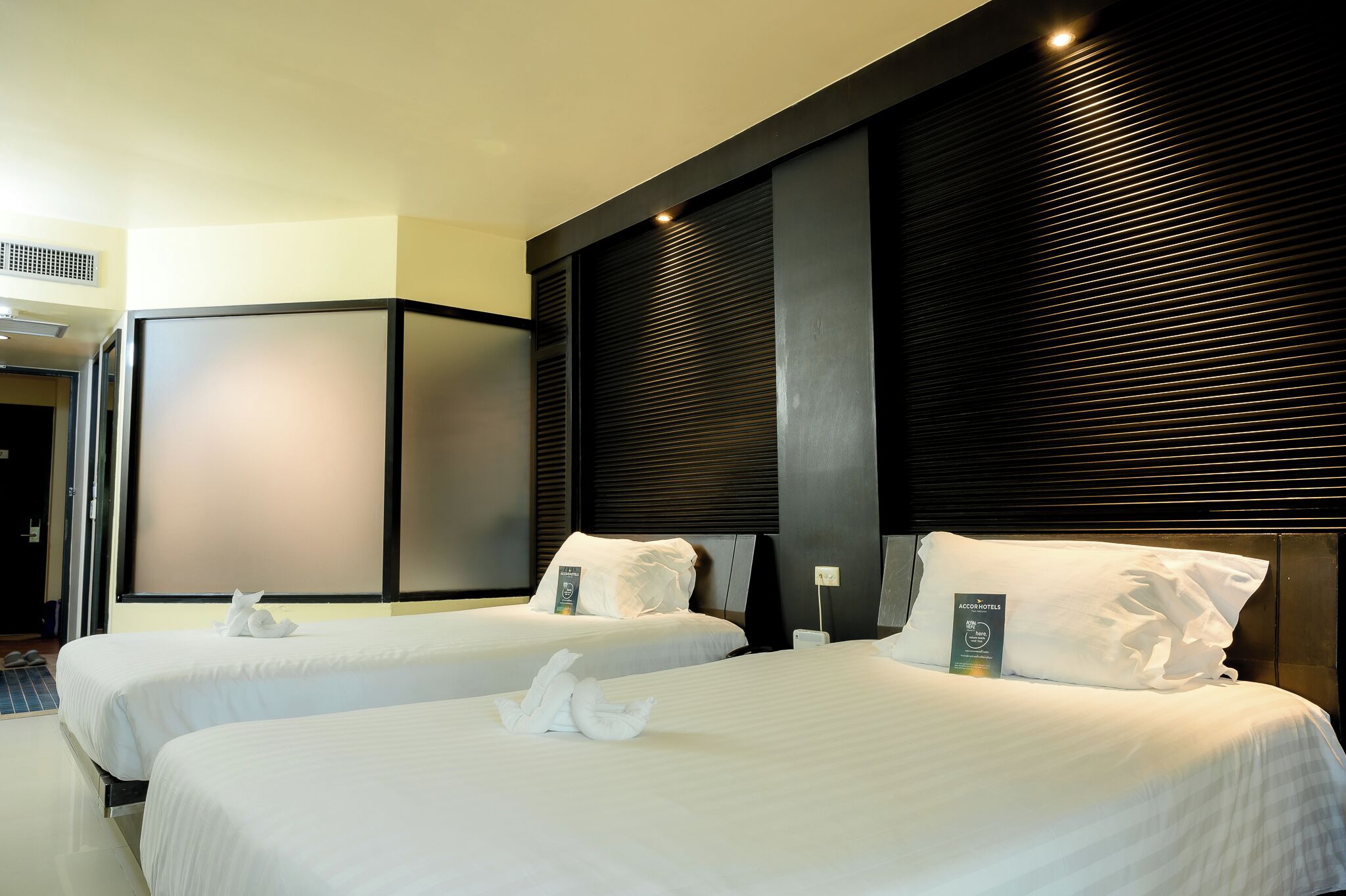 A hotel room with two beds, each with white linens and pillows, and a dark wood headboard.