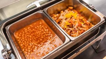 Un bufé con dos recipientes: uno con frijoles horneados y otro con un plato combinado de carne y verduras.
