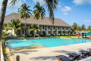 Un hotel con piscina, palmeras y una zona cubierta con sillones de descanso.
