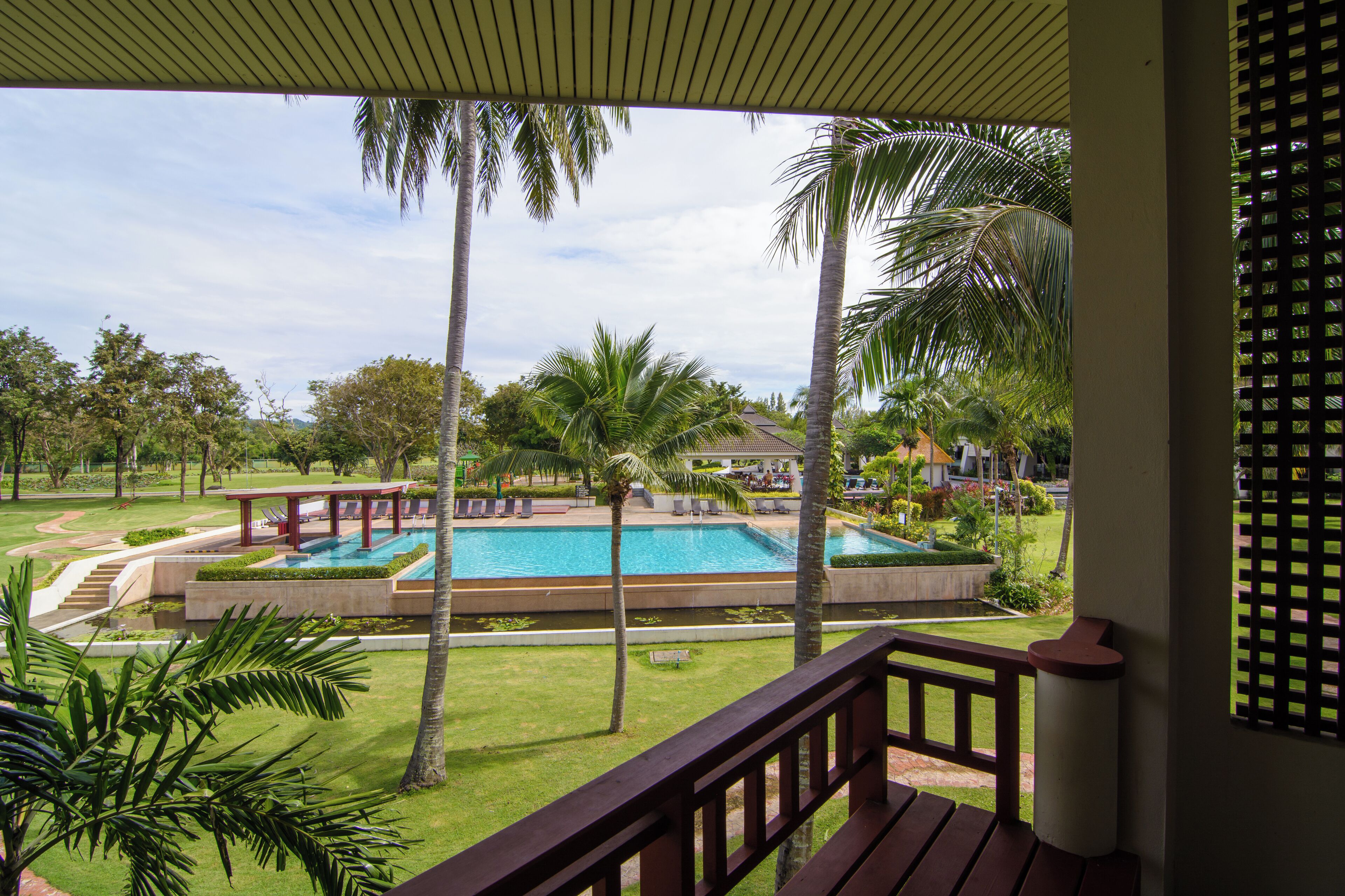A pool area with palm trees, a covered deck, and a view of a building in the background.