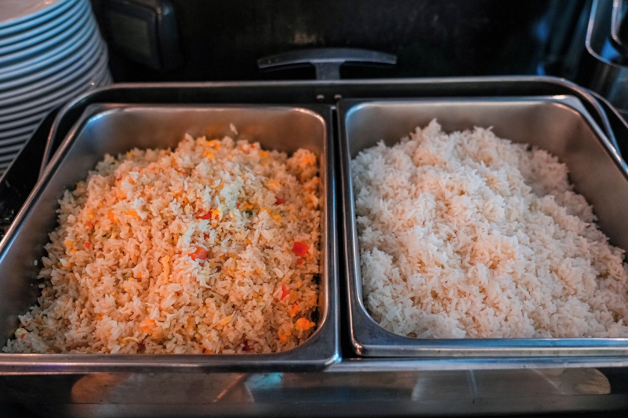 Two metal trays of fried rice, one with vegetables and the other plain.