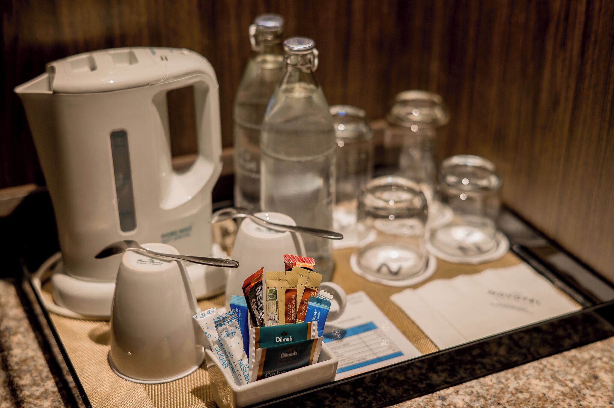Una bandeja amb una cafetera, tasses i un recipient que conté diversos productes de tocador.