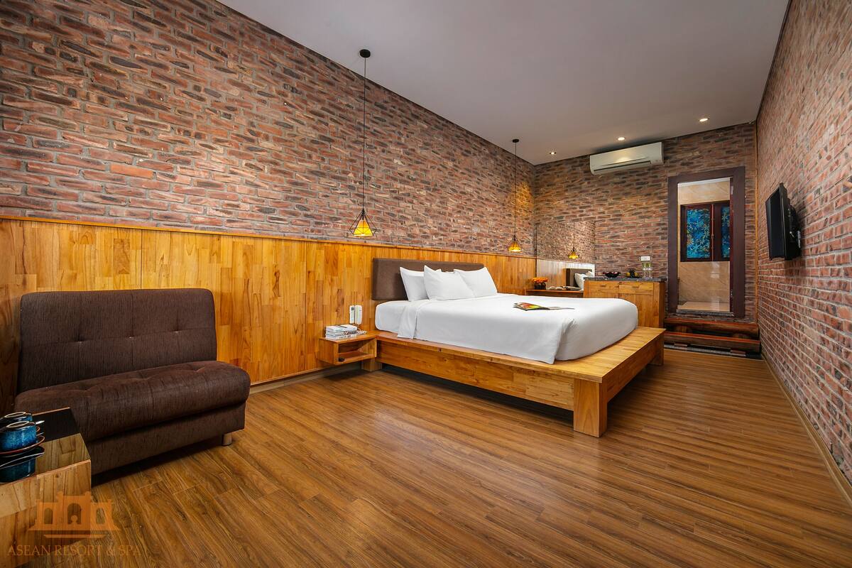 Une chambre moderne avec un mur en briques, un lambris en bois, un lit, un banc, une chaise et un téléviseur fixé au mur.