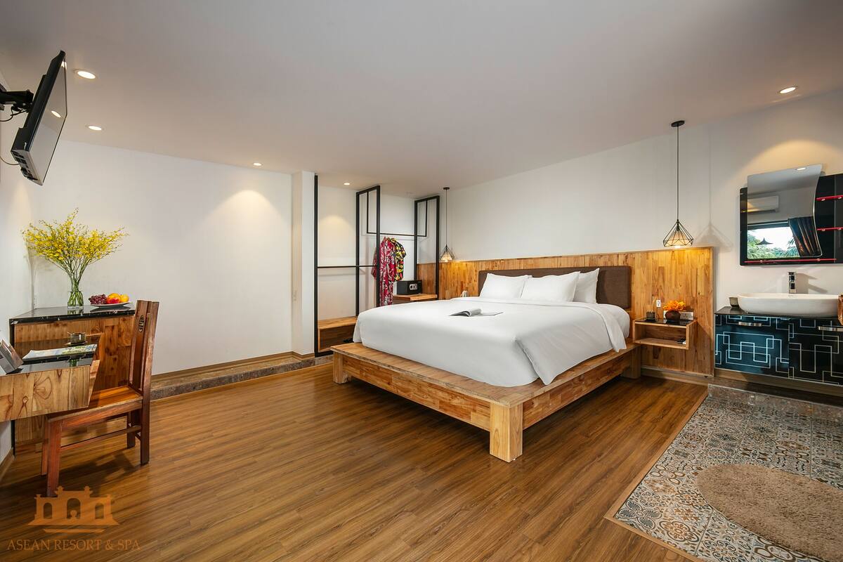 Une chambre à coucher moderne avec un lit en bois, des tables de chevet, un bureau et une salle de bain équipée d’un lavabo et d’un miroir.