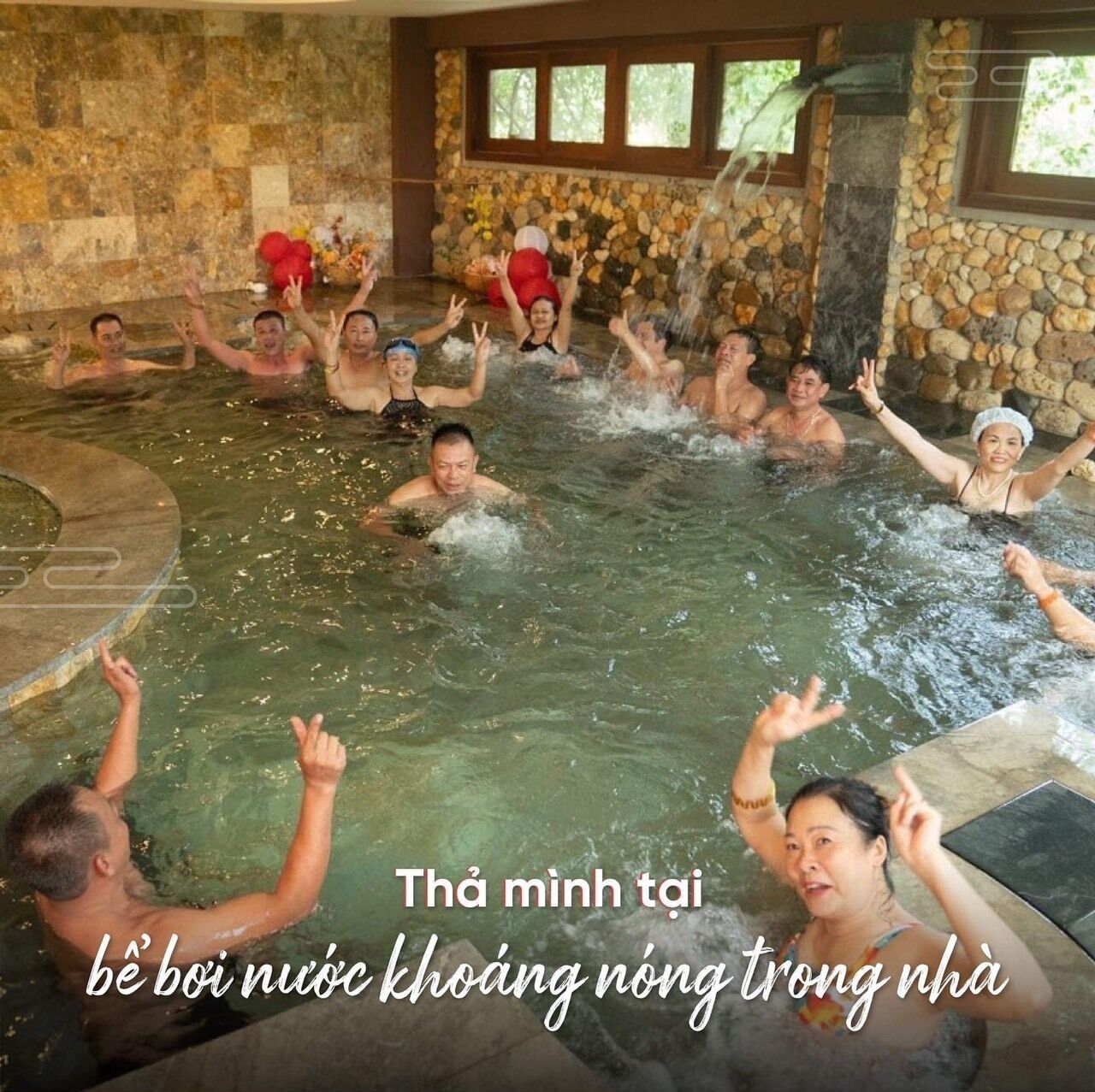 A group of people enjoying a hot tub in a stone-walled room with a view of trees outside.