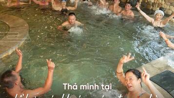 A group of people enjoying a hot tub in a stone-walled room with a view of trees outside.