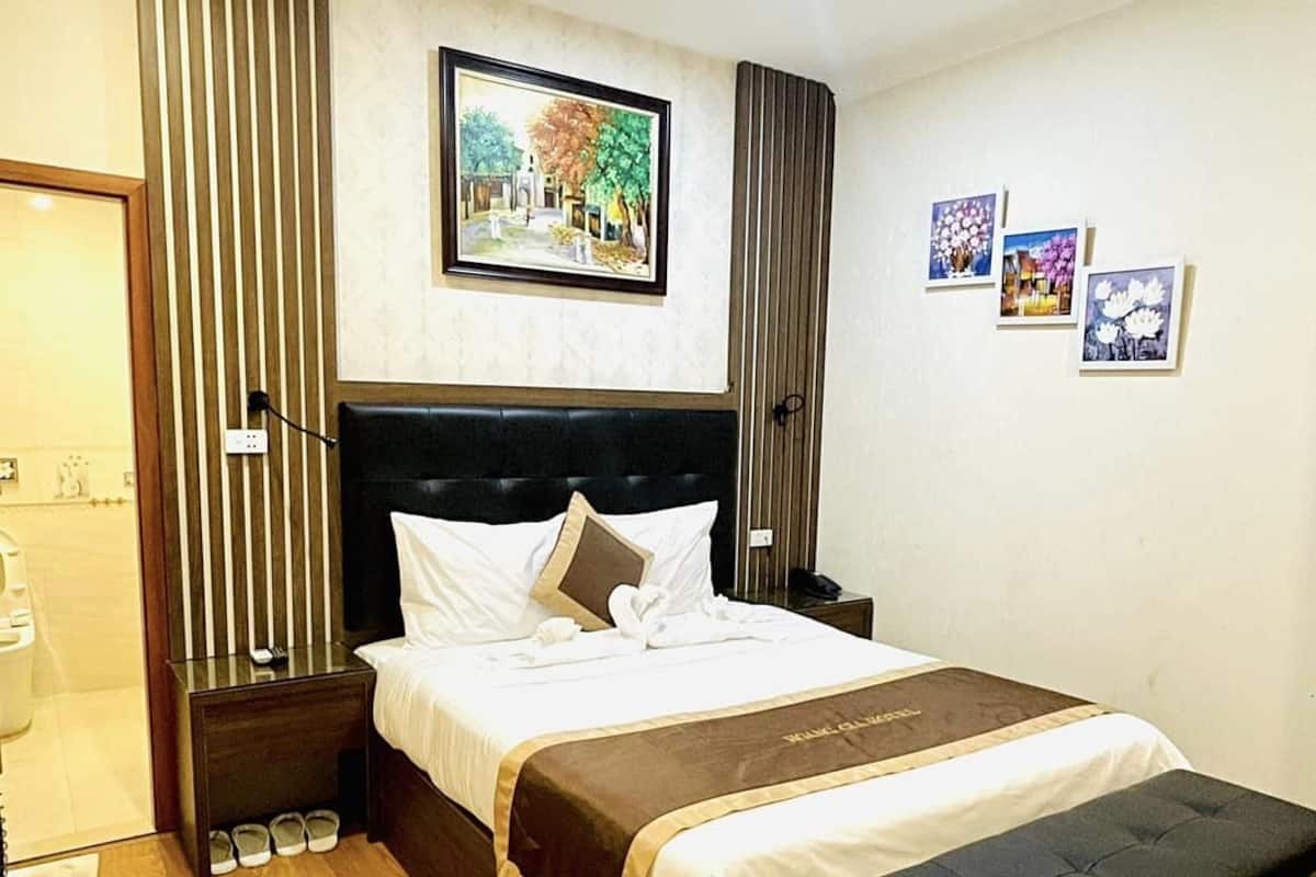 A hotel room with a large bed, a bedside table, a bench, and a wall-mounted painting.