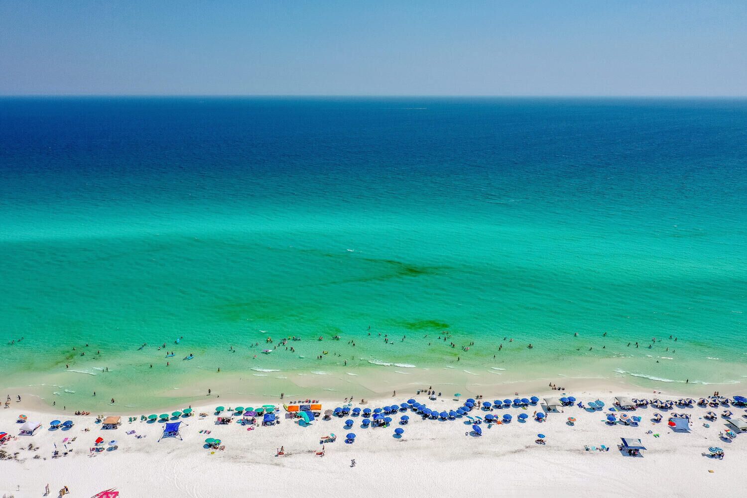 Een strand met helder turquoise water, wit zand en talloze parasols.