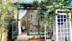 A covered outdoor seating area with a glass enclosure, a wooden bench, and a small table. - Lake View Homestay (Dien Hong)