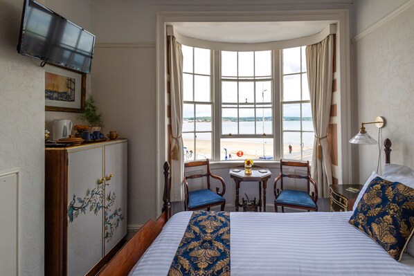 A hotel room with a bed, a desk, a chair, a table, and a window with a view of the sea.