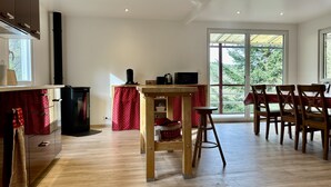 Une cuisine moderne avec un coin repas, un plancher en bois et de grandes fenêtres donnant sur un paysage verdoyant.