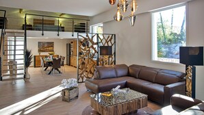 Un salon spacieux avec un canapé en cuir marron, une table basse en verre et un coin repas à l’arrière-plan.