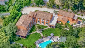 Un grand bâtiment à plusieurs étages, doté d’un toit en tuiles, entouré d’une végétation luxuriante et agrémenté d’une piscine.