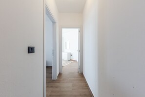 A narrow hallway with wooden flooring and white walls, leading to a room with a white door and a small window. - White Hill Suite by PS (Durrës)