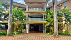 A multi-story hotel with a central entrance, surrounded by palm trees and a tiled walkway. - Nejobugg palace hotel (Arusha)