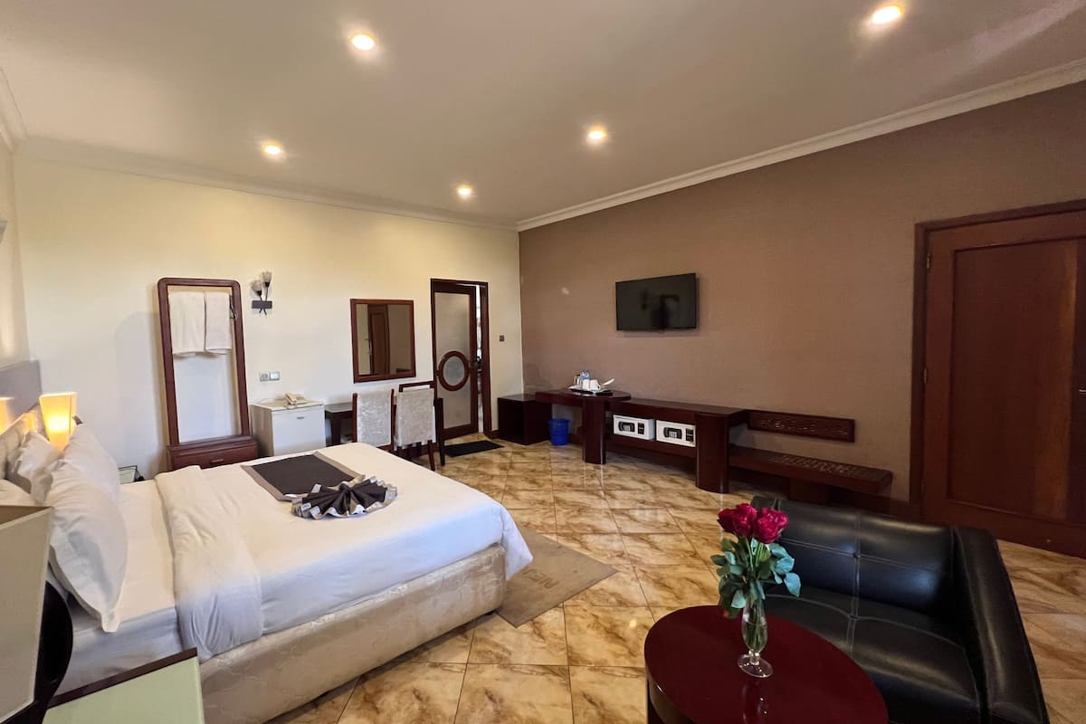 A hotel room with a bed, a desk, a chair, a TV, and a vase with flowers.