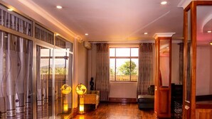 A spacious room with a wooden floor, large windows with curtains, a globe lamp, and a sofa. - Nejobugg palace hotel (Arusha)