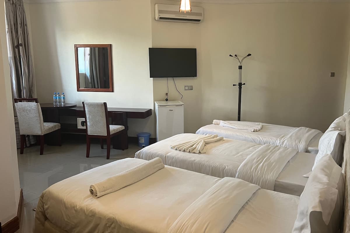 A hotel room with two beds, a desk, a chair, a TV, and a standing lamp.
